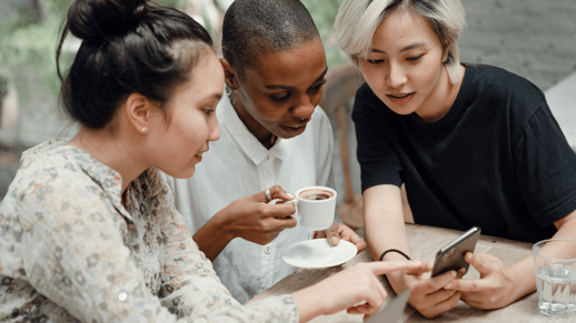 Three young people share coffee and focus on a smartphone screen