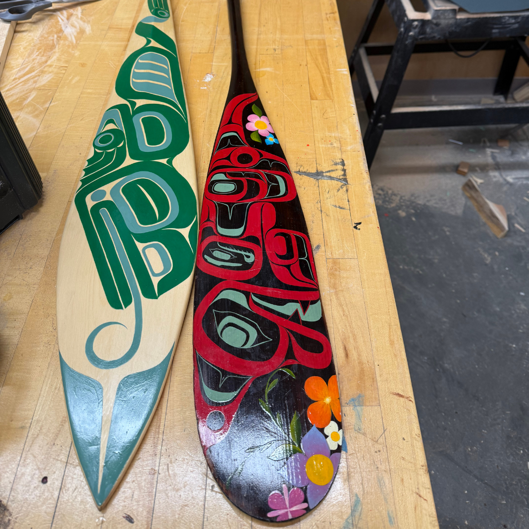 Deux rames en bois sculptées sur un établi avec des motifs peints à la main restaurés par l'artiste Jai Reid