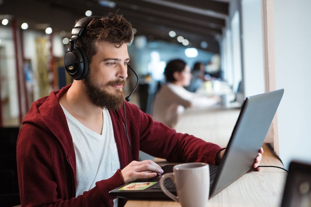 Concentrated handsome male with beard using headset and laptop.jpeg