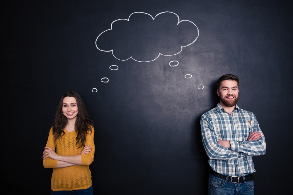 Happy couple standing with arms crossed and having the same thoughts over black board background.jpeg
