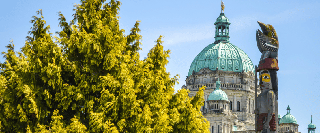 The Victoria Legislature building beside a totem pole.