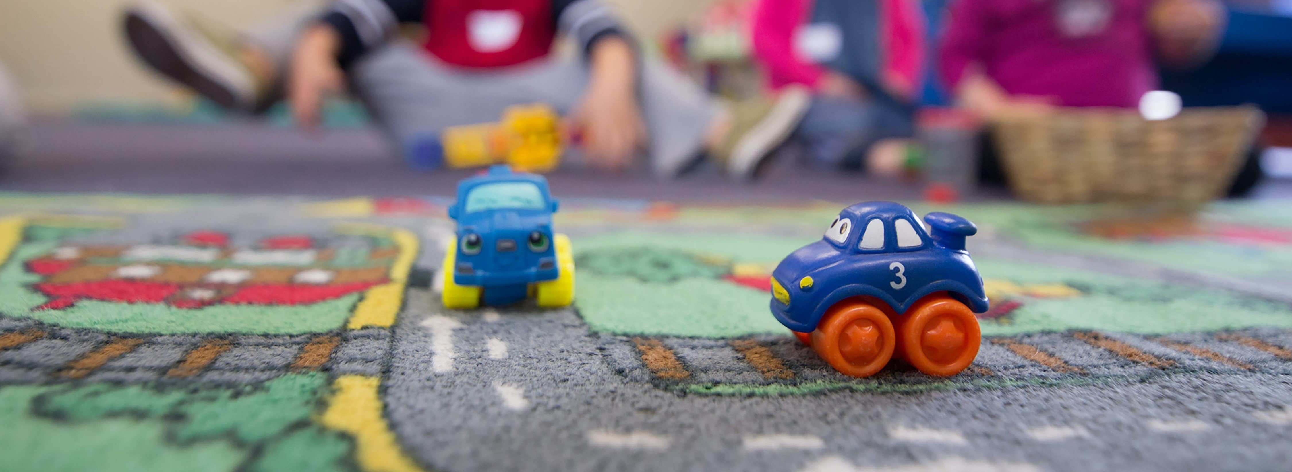 Image of children at a day care with toy cars in teh foreground