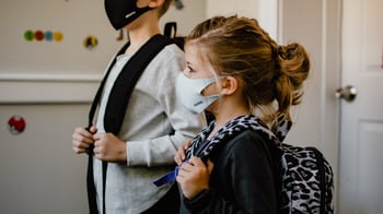 Two children in masks wearing backpacks