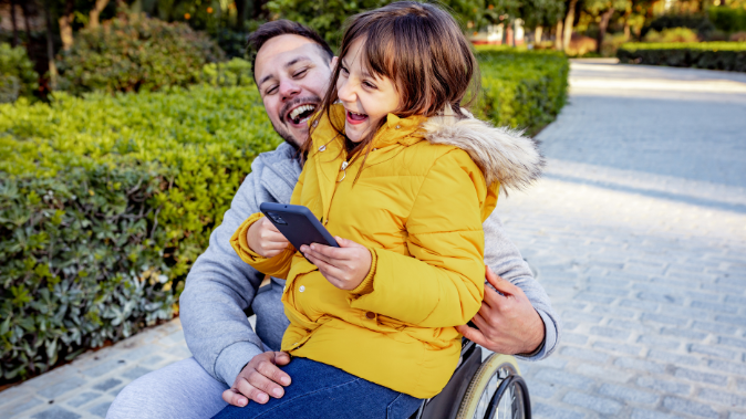 Man who uses wheelcheer with child on his lap, both laughing.