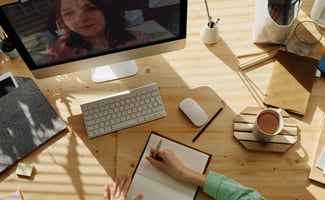 person writing in notebook with person on screen