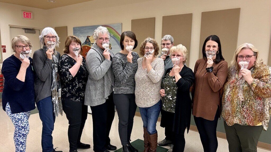 A group of people smiling and holding up chocolate moustaches. This is the team at Carman Wellness Connections.